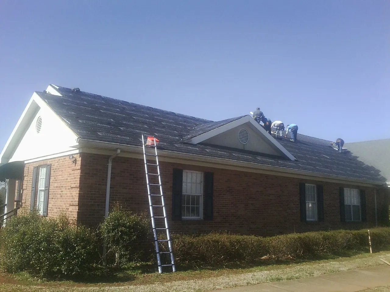 Crew tearing shingles off a brick ranch roof with a ladder set — Metal Roof Repair work by our crew in Speed