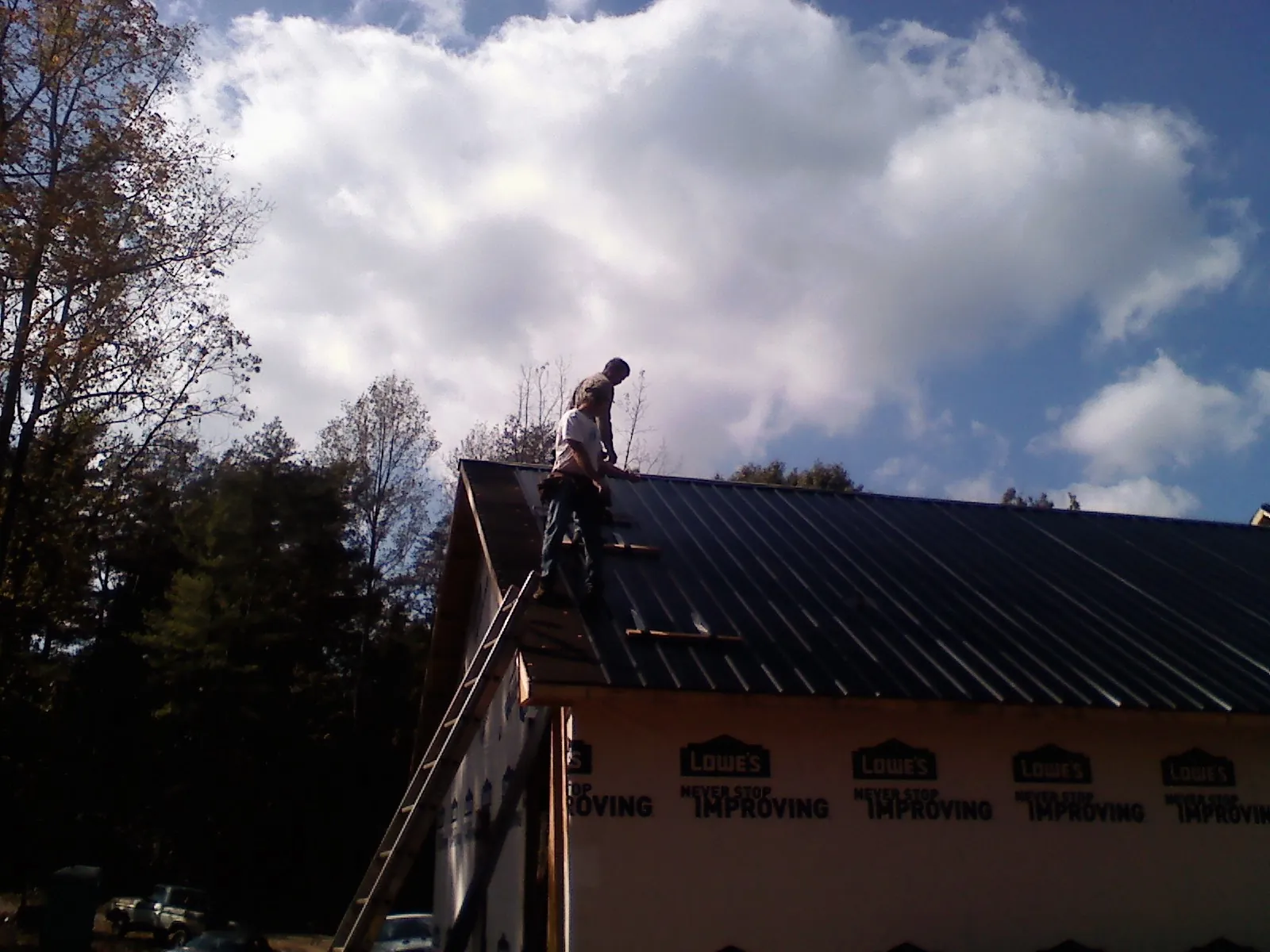 Roofer fastening dark metal panels high against a cloudy sky, from a Roof Inspection job in Speed